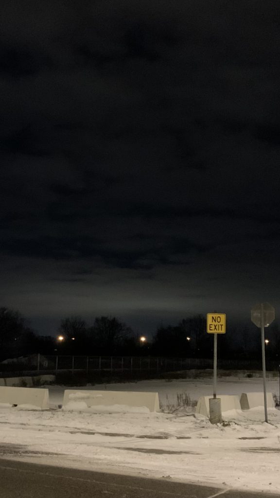 Night, dark trees and a cloudy sky. A street sign reads NO EXIT