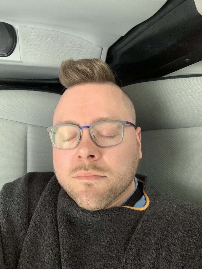 Me, lying on a car seat with my eyes closed, with a new haircut. 