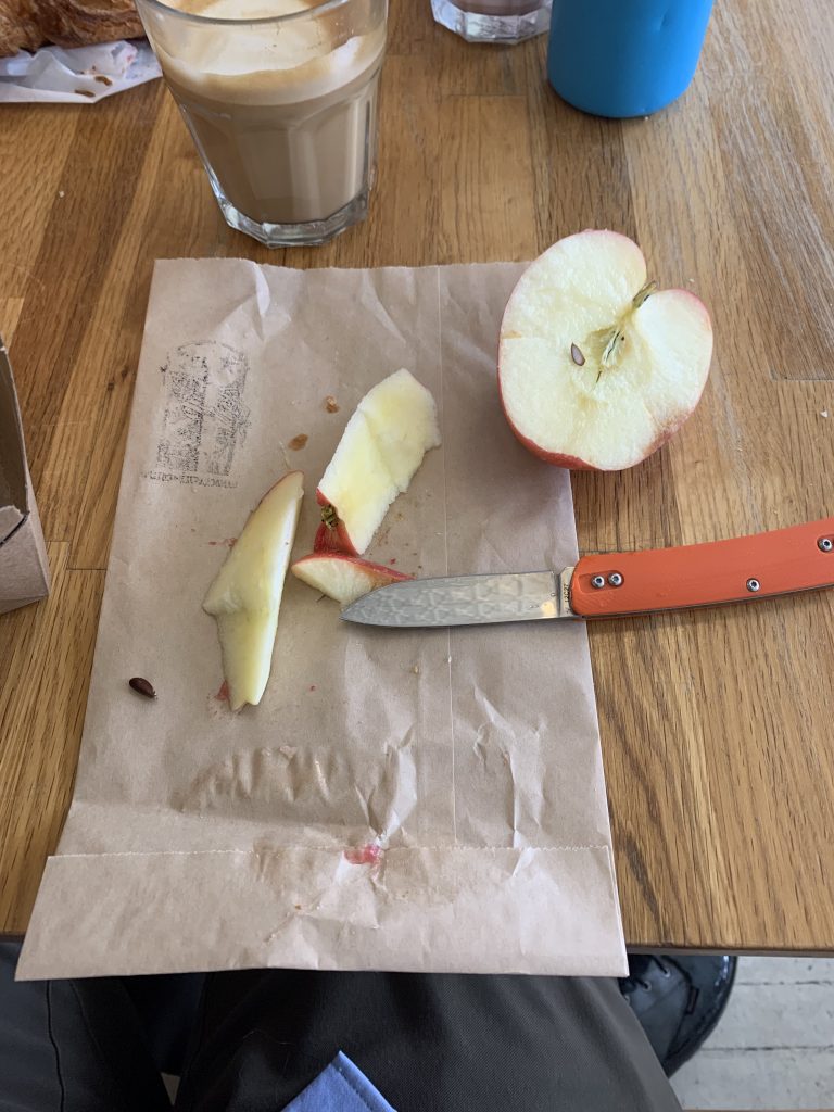 An open pocketknife, a sliced apple, a coffee. 