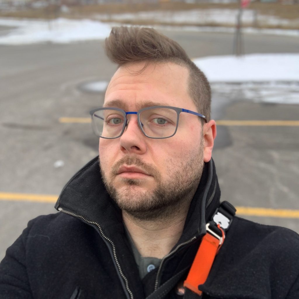 A portrait of me with a skeptical eyebrow raised, wearing my nice winter coat in a parking lot. 
